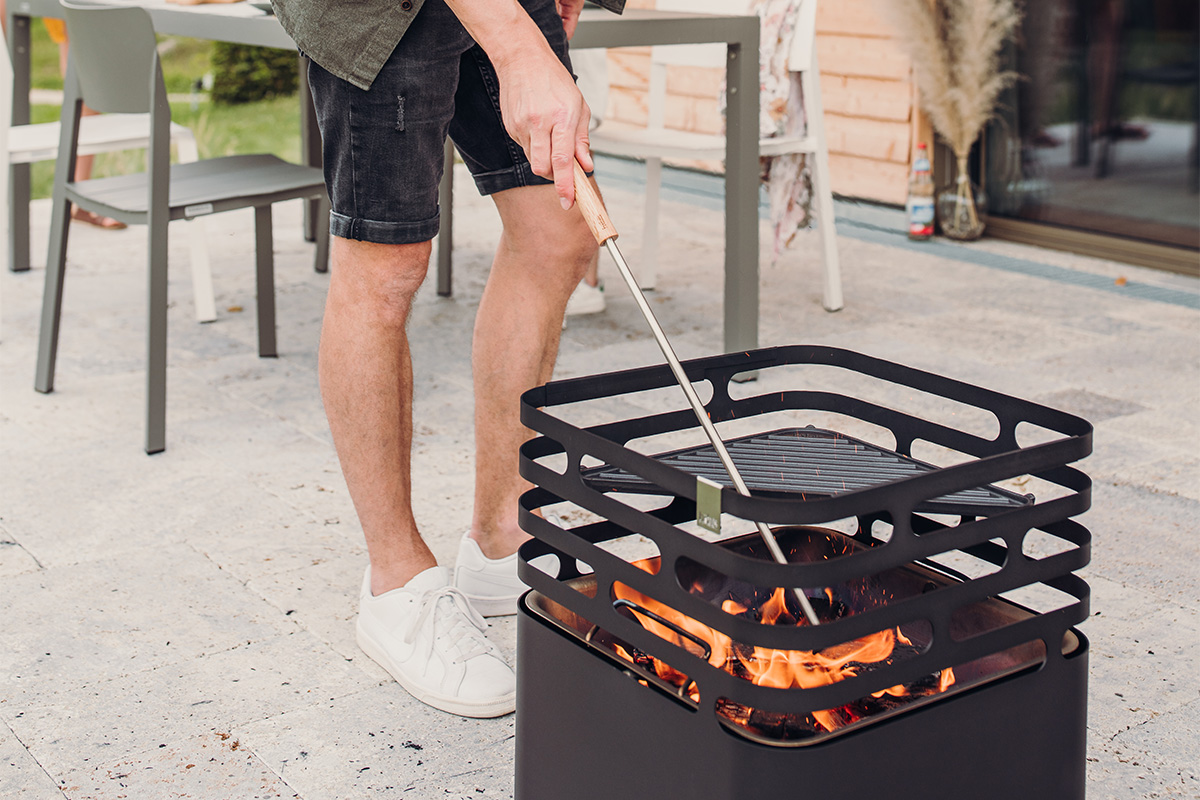 A man is cooking on a grill outside the 00251 Fire Tools Set 3 pcs complements the moment with its thoughtful design.