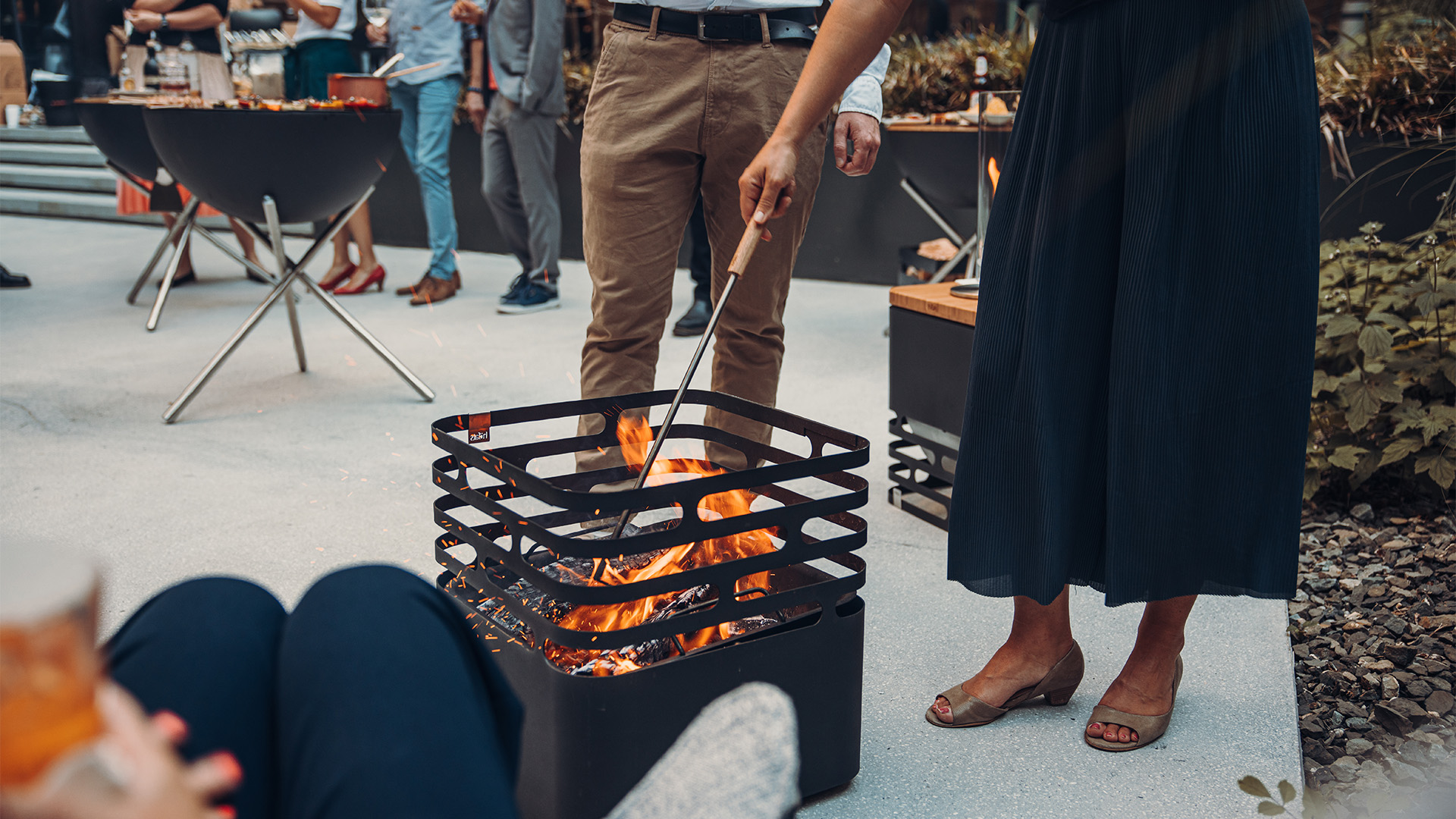 The 00252 Blow poker with stainless steel base is shown as a man and woman are standing around a fire pit, creating a stylish and accessible visual.