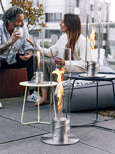 An inviting scene with a woman sitting on a bench, highlighted by the presence of the Spin 1500 Pedestal Fireplace