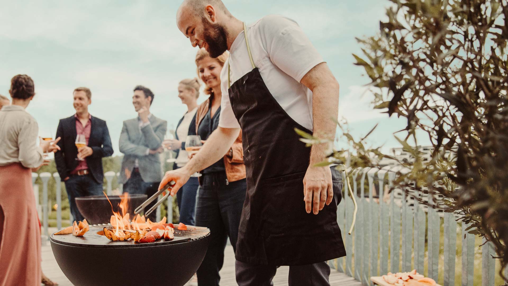 a man cooking food on a grill with people in the background