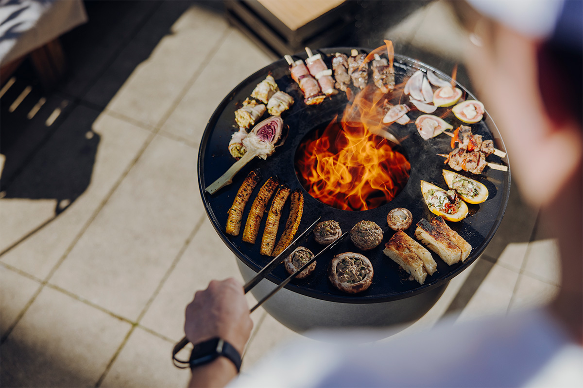 A person is cooking food on a grill, with the 00963 Moon 45 Plancha BBQ Set high adding a functional and elegant touch to the scene.