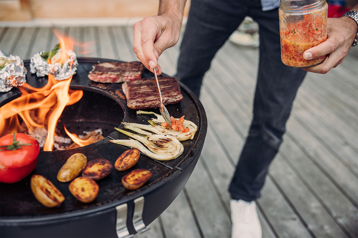 BOWL 57 Plancha A man is cooking food on a grill, with the 00256 Bowl 57 Plancha adding a functional and elegant touch to the scene.