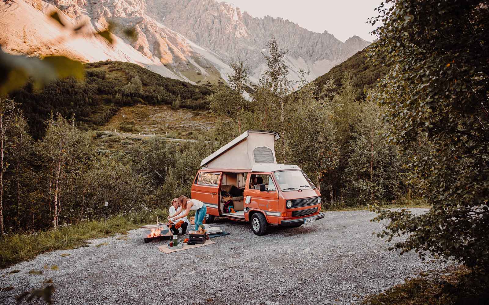 a van parked on a gravel road with a camper van in the background.