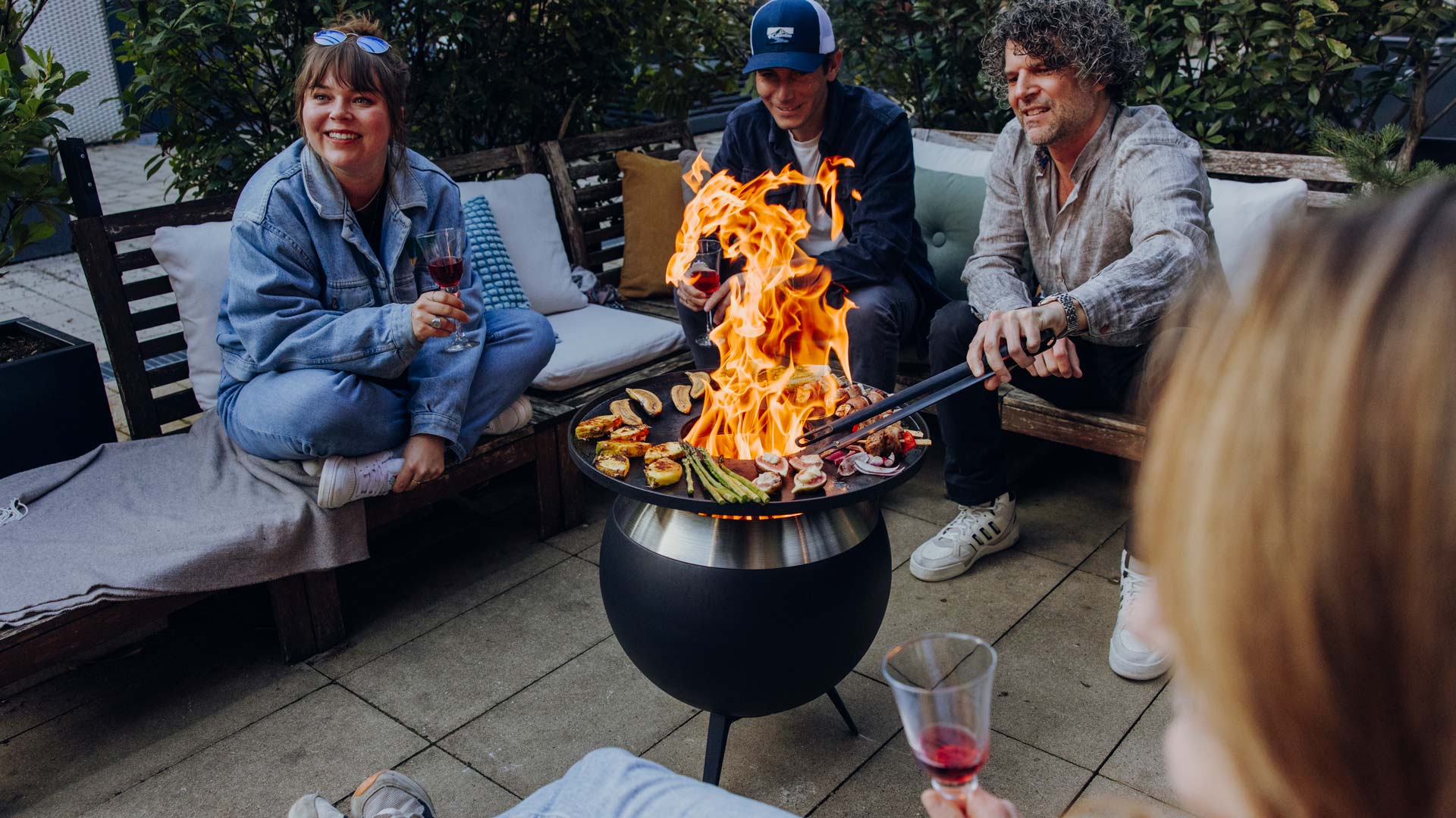 The Moon 45 Plancha BBQ set low is featured in a thoughtfully styled setting, showing a group of people sitting around a fire pit