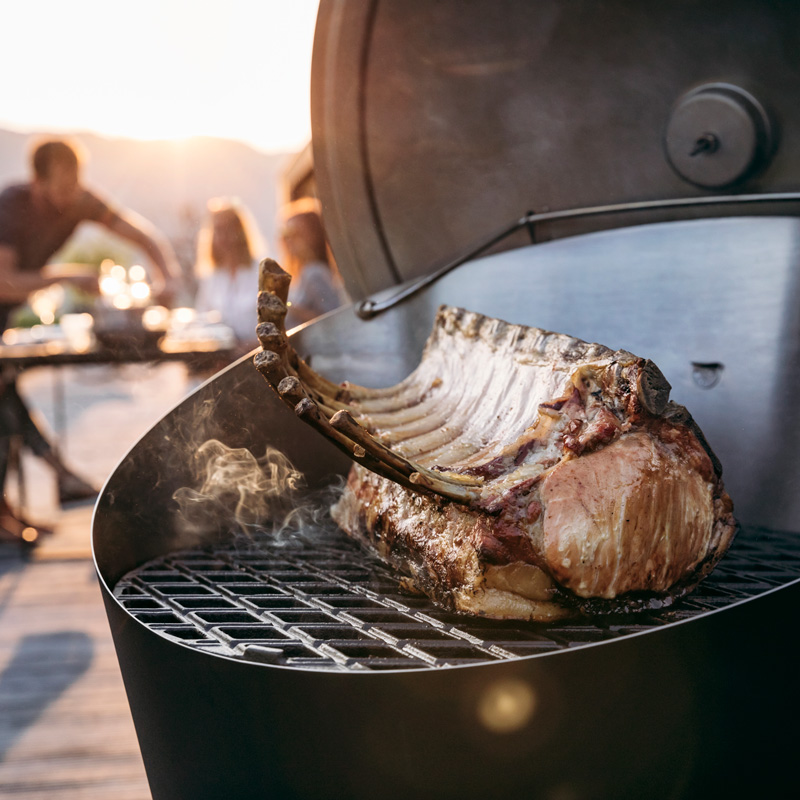 Illustrated is a person is grilling a chicken on a grill, with the CONE Charcoal Grill.