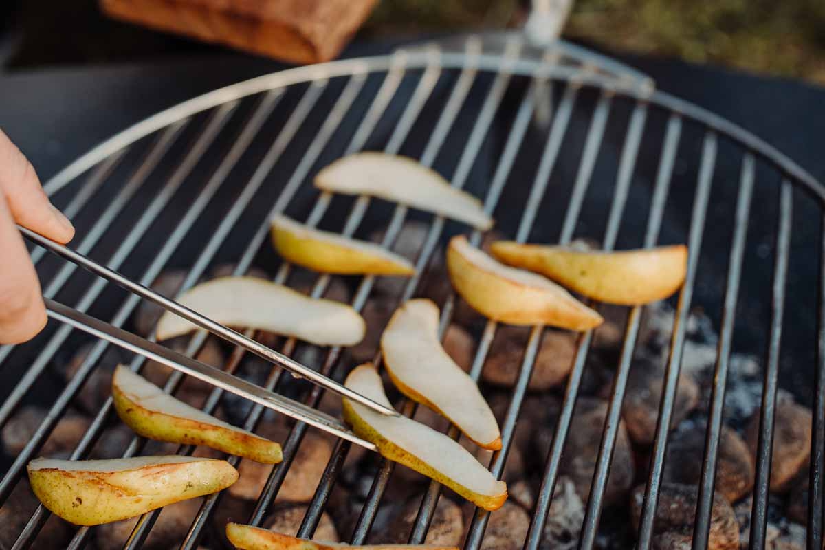 Someone using a tong to remove the potatoes from the grill, with the Triple 65 Fireplace BBQ Set adding a functional and elegant touch to the scene.