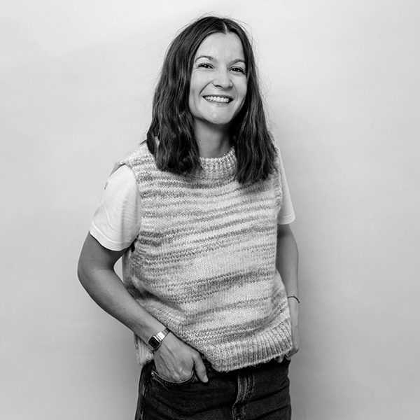 a woman in a sweater and jeans standing against a wall.
