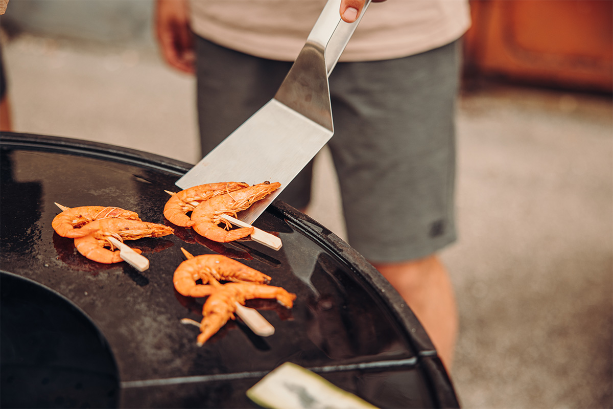 Spatula An inviting scene with a person is cutting a piece of food on a grill, highlighted by the presence of the 00473 Spatula.