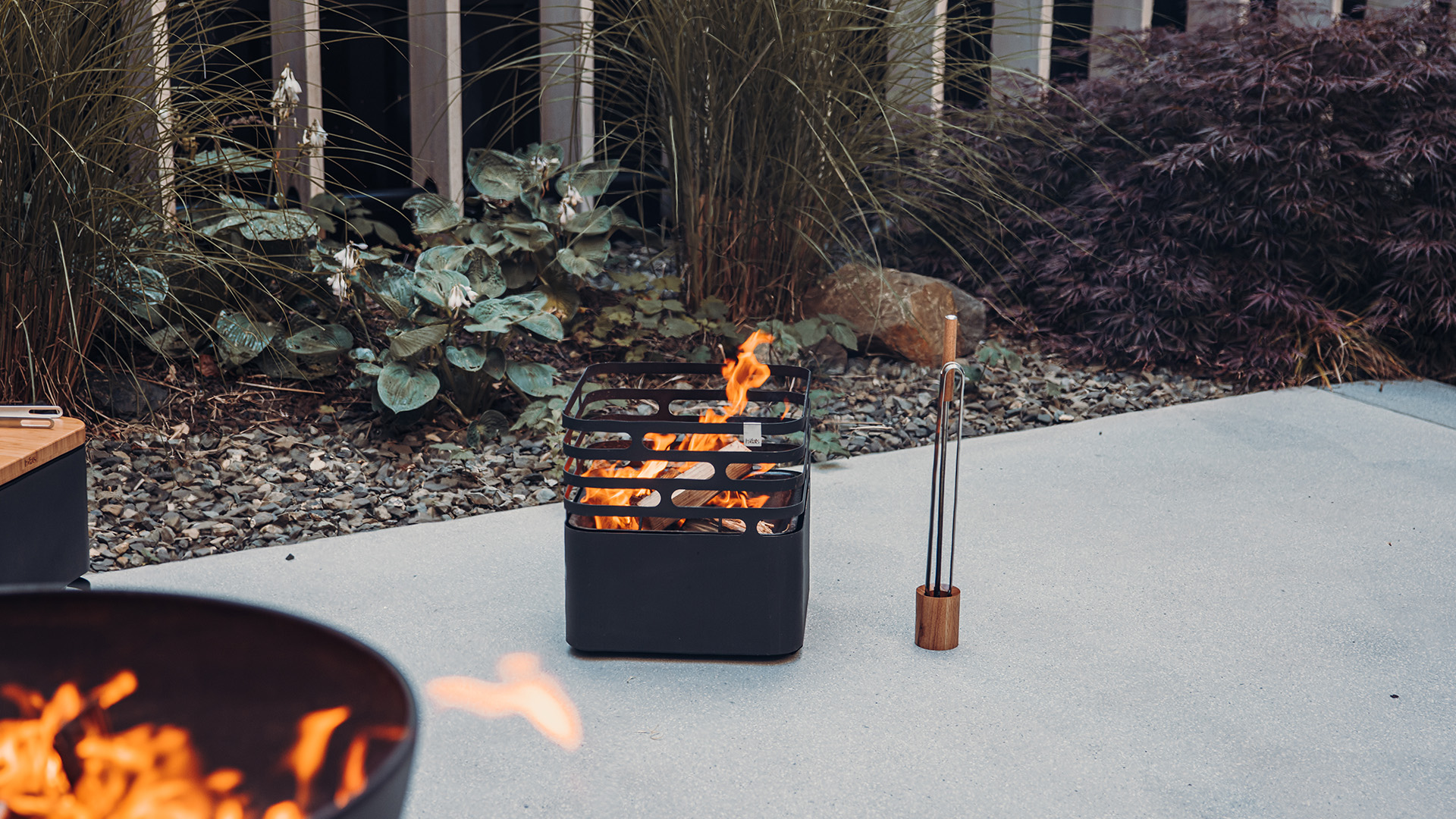 Depicted here is a fire pit with a fire burning in it, with the Wooden Base for Blow Poker and Fire Tongs.