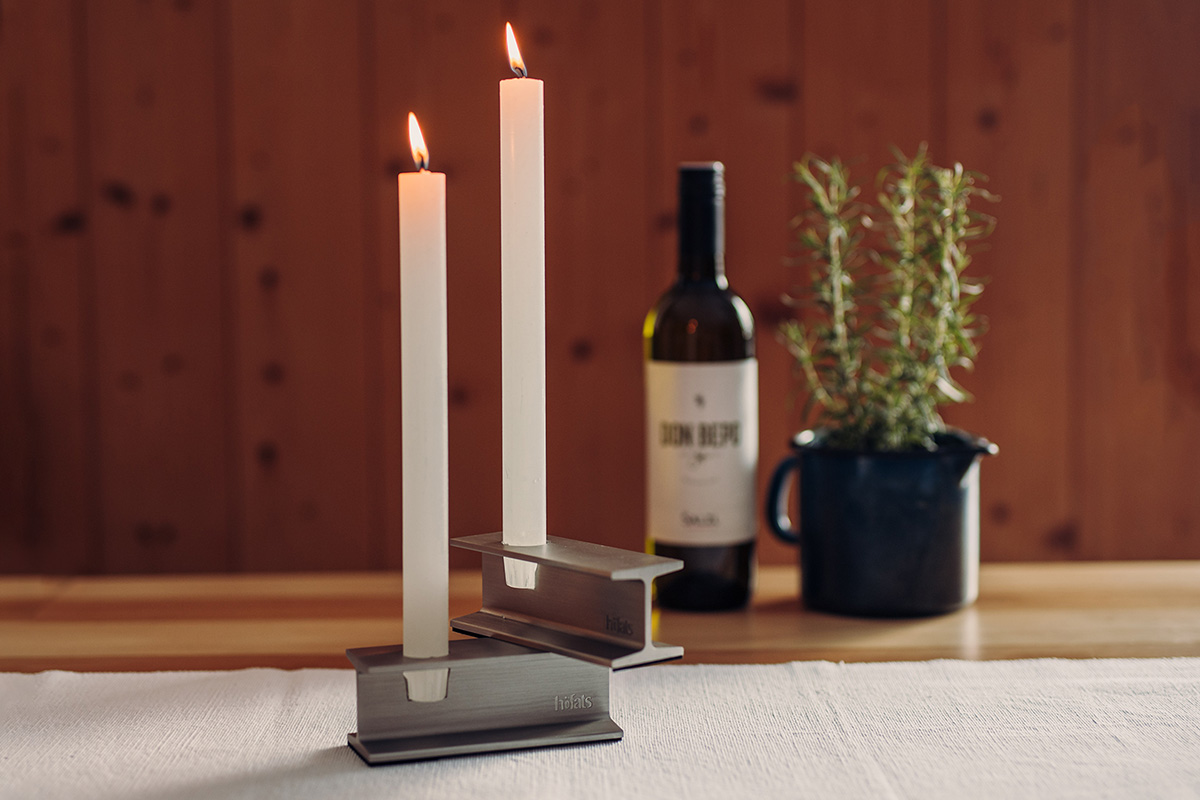 Illustrated is a candle and a bottle of wine on a table, with the HENRY METAL I Candleholder silver.