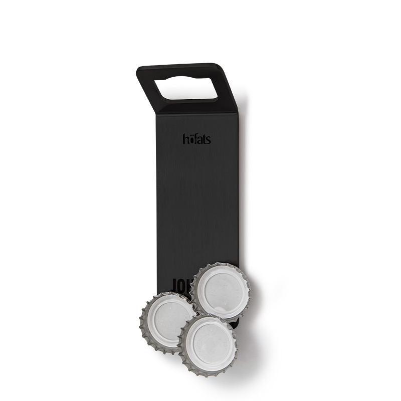 The 00841 Johnny Catch Magnet Black Bottleopener is shown as a bottle opener with bottle caps sticking to it, creating a stylish and accessible visual.