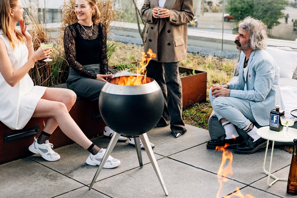 A group of people sitting around a fire pit the 00717 Moon 45 with high stand complements the moment with its thoughtful design.
