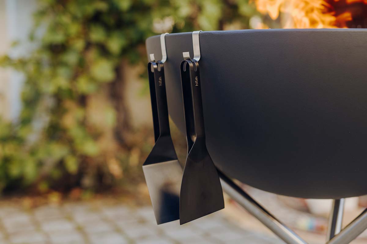 A black fire pit with a fire in the background the 00857 Scraper black complements the moment with its thoughtful design.