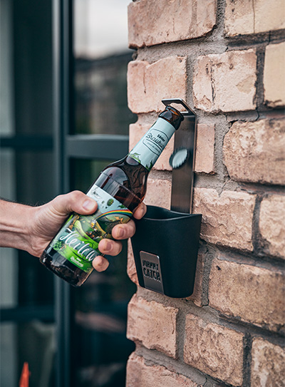 This image shows a man opening a bottle of beer from a wall, with the JOHNNY CATCH Cup.