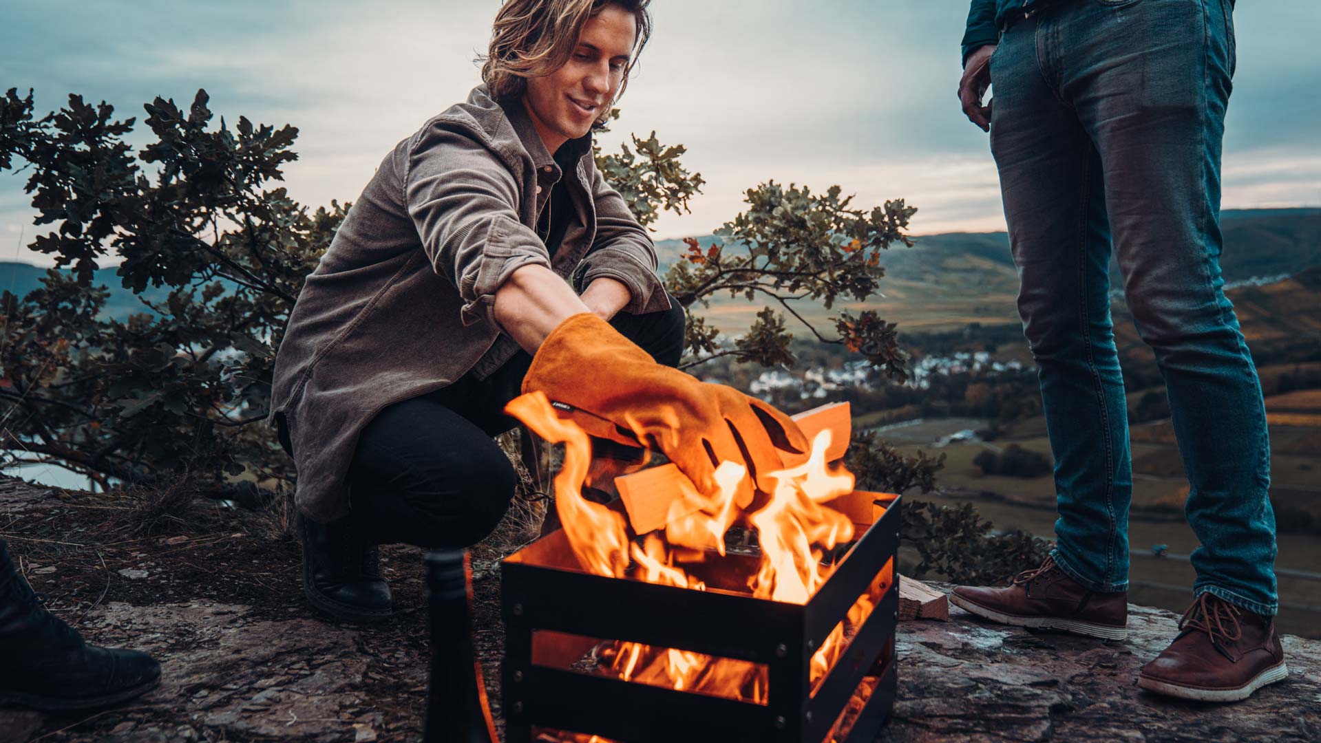 A woman sitting on a rock by a fire, enriched by the presence of the Glove Tools, which merges design with utility.