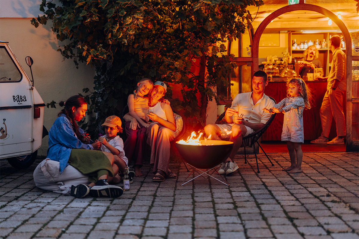 Scene showing a group of people sitting around a fire pit, where the 00249 Bowl 57 with starstand stands out for its practical elegance.