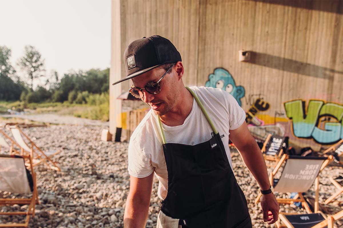CAP black a man in an apron and hat standing on the beach.