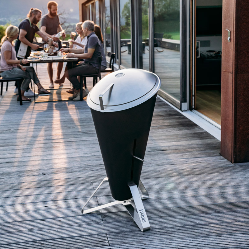The photo presents a black and silver bbq grill on a wooden deck, with the CONE Charcoal Grill.