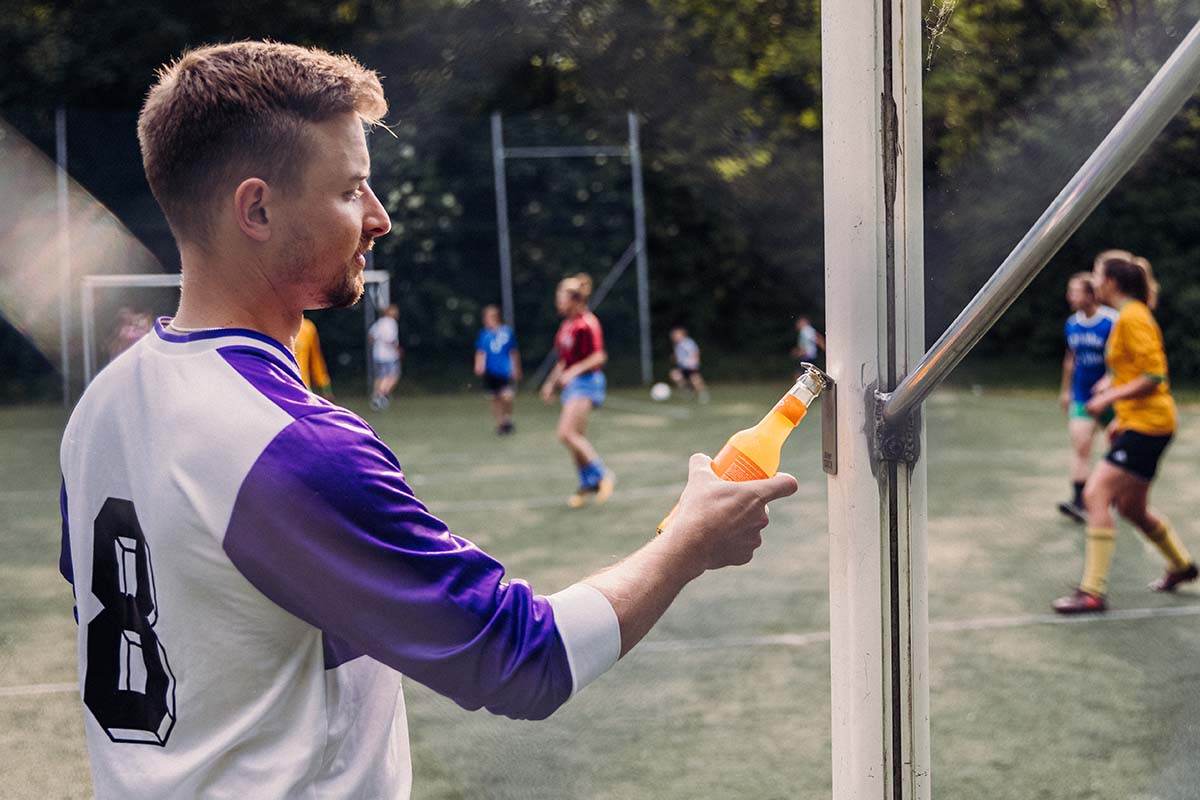 A man holding an orange drink openin the bottle. the Johnny Catch Magnet Bottleopener complements the moment with its thoughtful design.